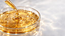 Macro scientifica: capsula Petri con liquido resinoso color miele, pipetta di vetro che rilascia una goccia dorata e sfere molecolari sospese, simbolo della propoli purificante, Chrissie Cosmetics