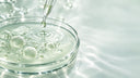 Capsula Petri di vetro con liquido verde salvia, bolle e pipetta che rilascia una goccia, macro scientifica sul microbioma cutaneo, Chrissie Cosmetics